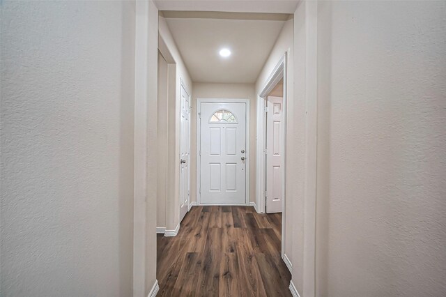 hallway with dark wood-style flooring, a textured wall, and baseboards