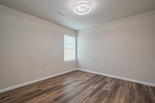 unfurnished room featuring dark wood-style flooring, visible vents, and baseboards