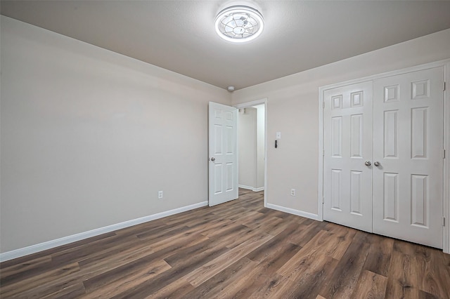 unfurnished bedroom featuring baseboards, dark wood finished floors, and a closet