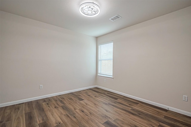 empty room featuring dark wood-type flooring, visible vents, and baseboards