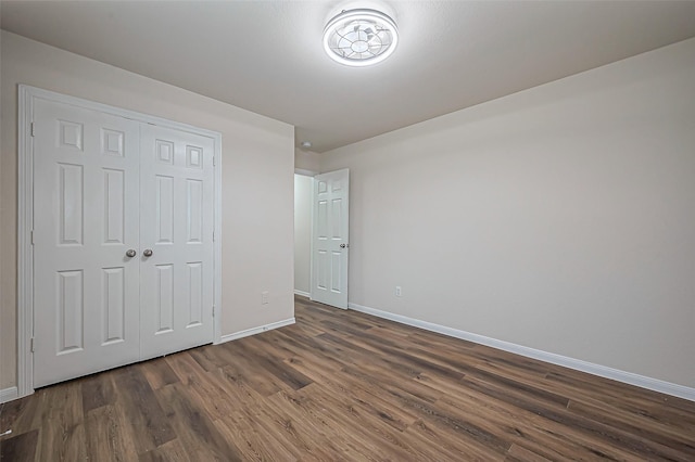 unfurnished bedroom with a closet, baseboards, and dark wood-style flooring