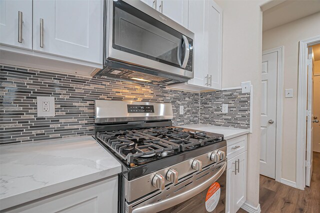 kitchen featuring dark wood-style floors, appliances with stainless steel finishes, light stone countertops, white cabinetry, and backsplash