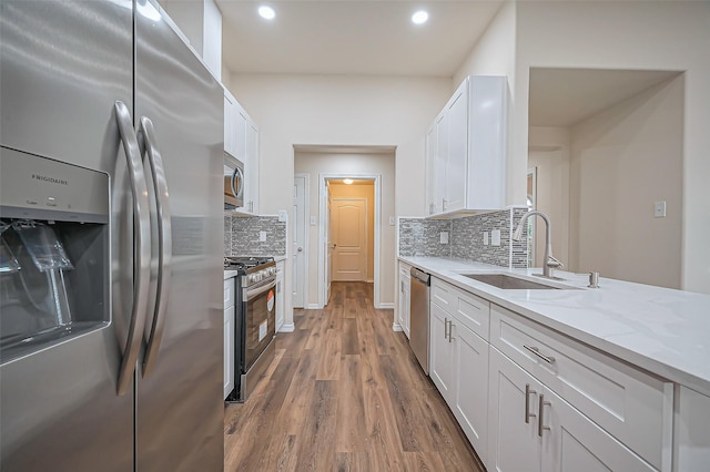 kitchen with light stone counters, appliances with stainless steel finishes, white cabinets, a sink, and wood finished floors