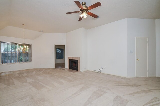 unfurnished living room featuring carpet, vaulted ceiling, a tiled fireplace, and ceiling fan with notable chandelier