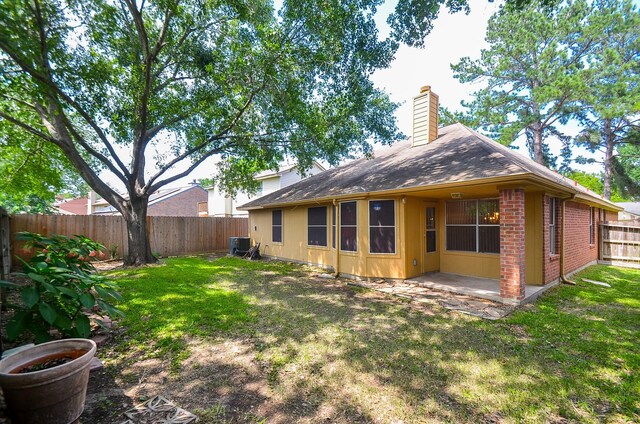 rear view of house featuring brick siding, a yard, a chimney, a patio, and a fenced backyard