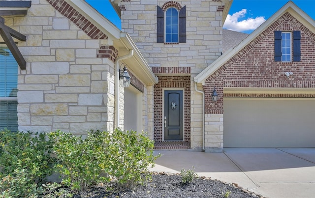 entrance to property with brick siding, roof with shingles, an attached garage, stone siding, and driveway