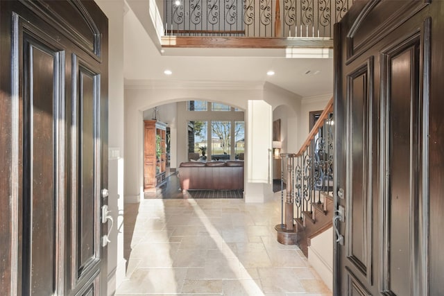 entrance foyer with arched walkways, stone tile flooring, a towering ceiling, and ornamental molding