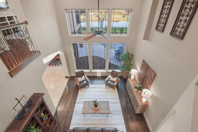 living room featuring wood finished floors, baseboards, a towering ceiling, and ceiling fan