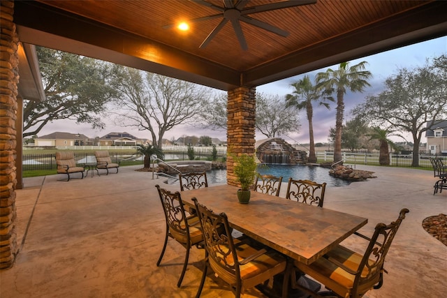 patio terrace at dusk featuring a ceiling fan, a jacuzzi, a fenced backyard, a community pool, and outdoor dining area