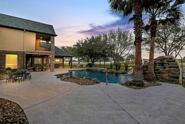 pool at dusk with a patio area and an outdoor pool