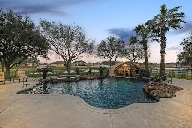 view of swimming pool featuring a patio area, fence, a water slide, and a pool with connected hot tub