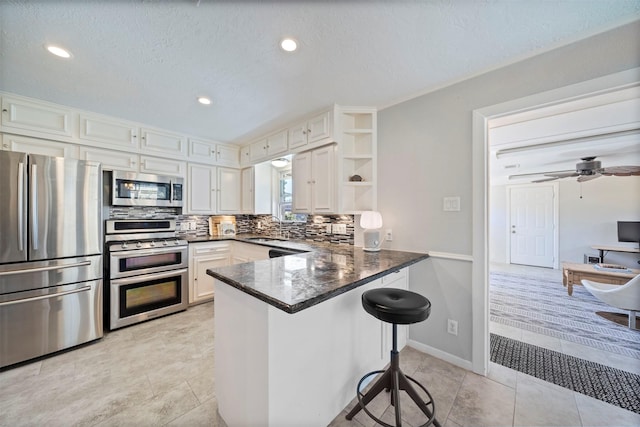 kitchen with dark countertops, a peninsula, white cabinets, stainless steel appliances, and open shelves