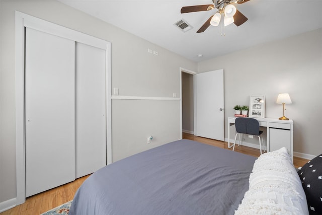 bedroom featuring a ceiling fan, wood finished floors, visible vents, baseboards, and a closet