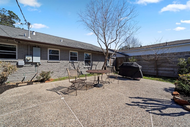 back of house featuring stone siding, fence, a shingled roof, and a patio area