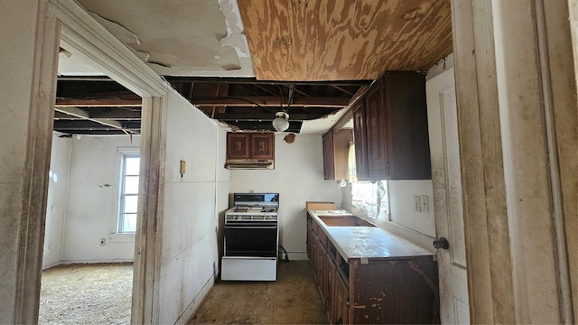 kitchen with range with gas cooktop, light countertops, a sink, dark brown cabinets, and under cabinet range hood