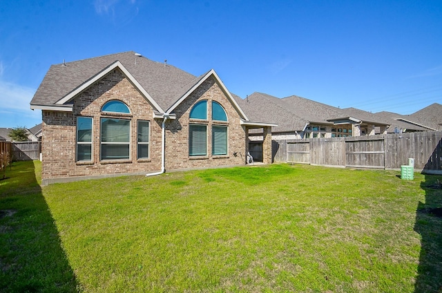 back of house featuring roof with shingles, brick siding, a lawn, and a fenced backyard