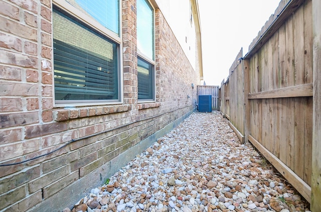 view of side of property featuring brick siding, cooling unit, and fence