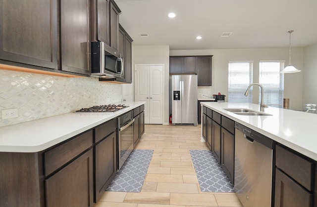 kitchen featuring dark brown cabinetry, decorative backsplash, appliances with stainless steel finishes, light countertops, and a sink