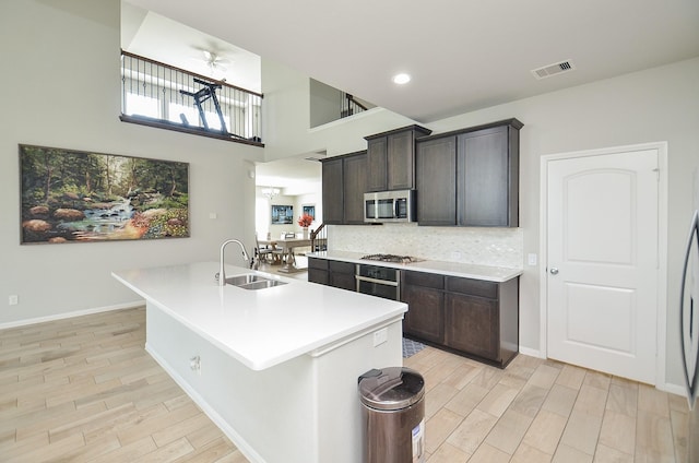 kitchen with tasteful backsplash, light countertops, appliances with stainless steel finishes, light wood-style floors, and a sink