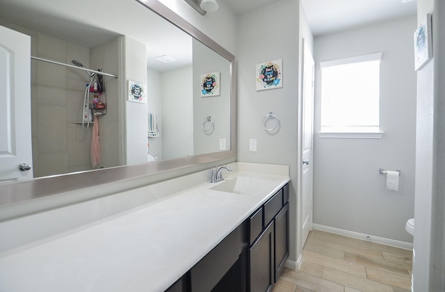 bathroom with toilet, vanity, wood finished floors, baseboards, and walk in shower