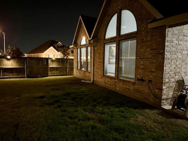 property exterior at night with a yard, brick siding, and fence