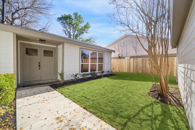 view of exterior entry with a lawn and fence