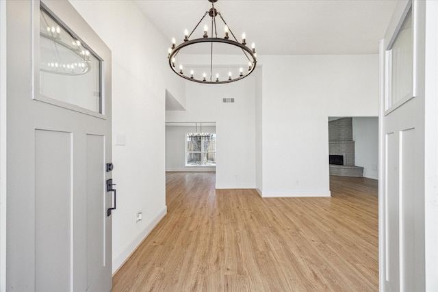 entryway featuring baseboards, a towering ceiling, light wood-type flooring, a fireplace, and a chandelier