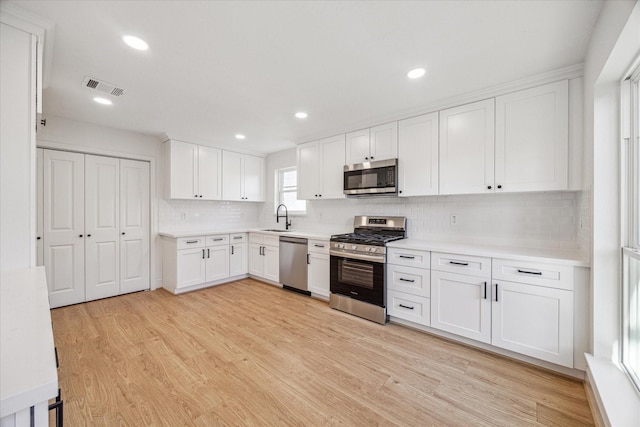 kitchen with visible vents, white cabinets, light wood-style flooring, stainless steel appliances, and a sink