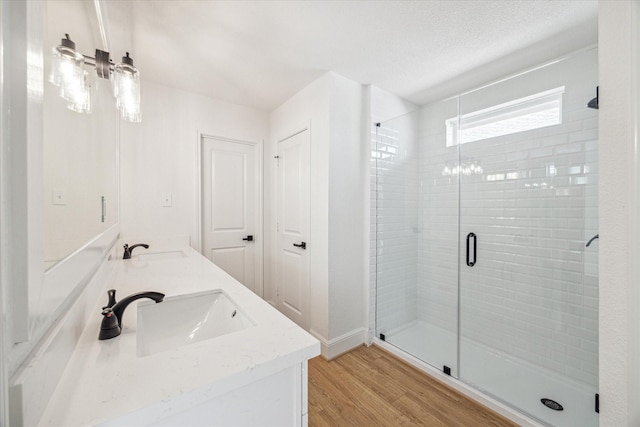 full bath with double vanity, a shower stall, a sink, and wood finished floors