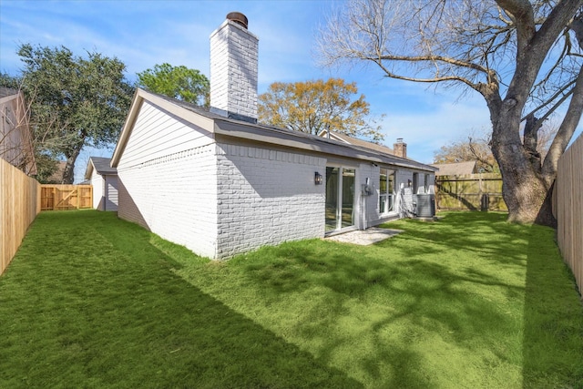 back of property featuring brick siding, a chimney, a fenced backyard, and a lawn