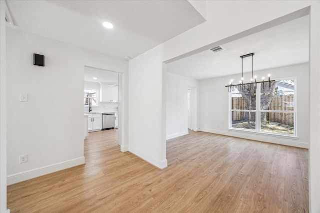 unfurnished dining area with light wood-type flooring, a healthy amount of sunlight, visible vents, and an inviting chandelier