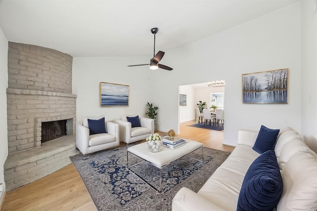 living area with vaulted ceiling, a brick fireplace, wood finished floors, and a ceiling fan