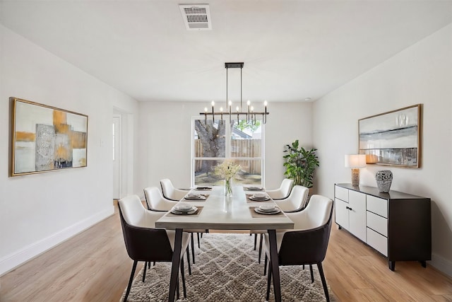 dining space with baseboards, light wood-style flooring, visible vents, and an inviting chandelier