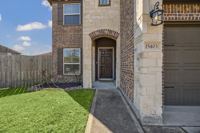 view of exterior entry featuring a garage, stone siding, brick siding, and fence