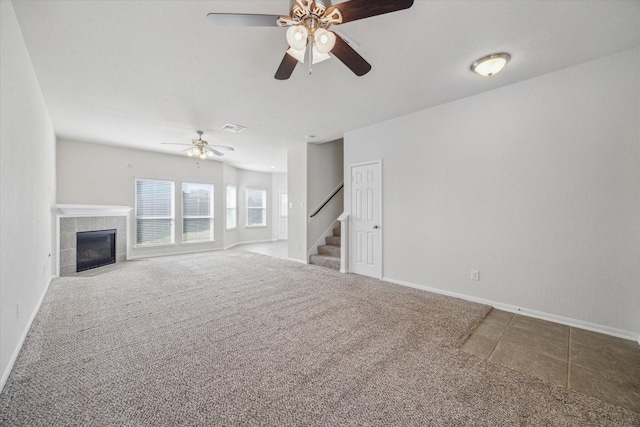 unfurnished living room featuring a tile fireplace, carpet floors, visible vents, baseboards, and stairs