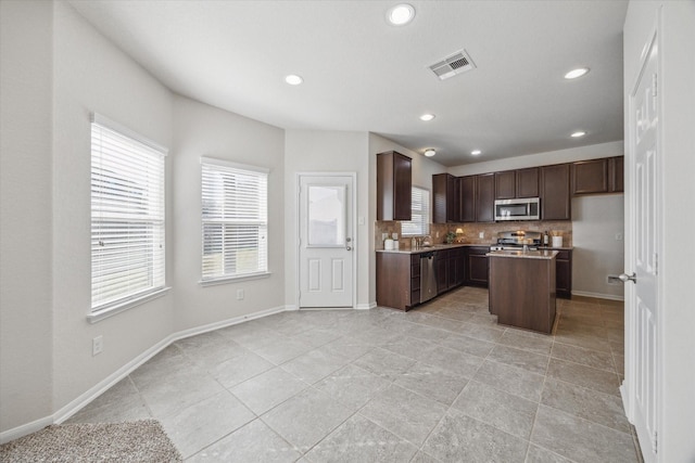 kitchen with stainless steel appliances, visible vents, baseboards, dark brown cabinets, and backsplash