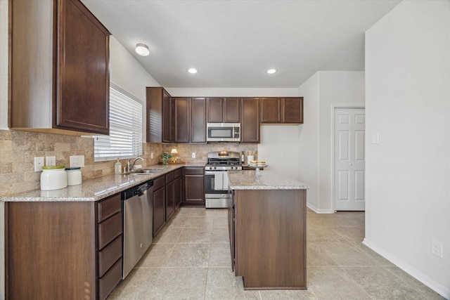 kitchen featuring baseboards, appliances with stainless steel finishes, backsplash, a center island, and a sink