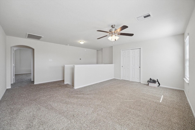 carpeted spare room featuring ceiling fan, visible vents, arched walkways, and baseboards