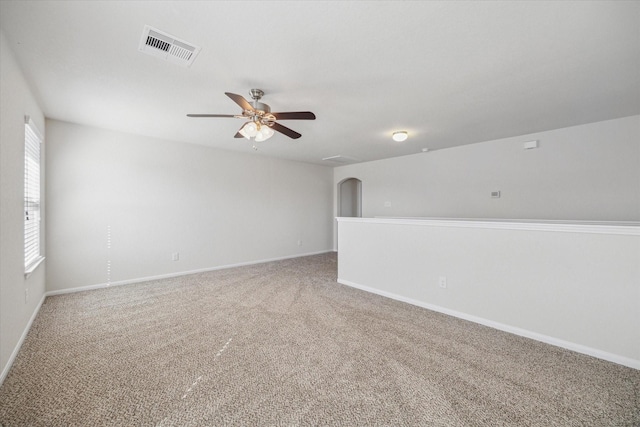 carpeted spare room with ceiling fan, arched walkways, visible vents, and baseboards