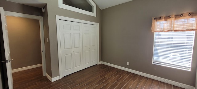 unfurnished bedroom with dark wood-type flooring, a closet, multiple windows, and baseboards