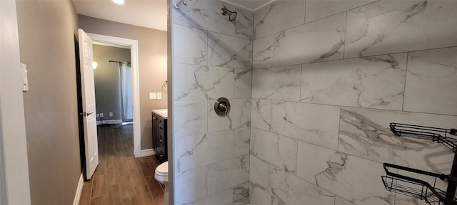 full bathroom featuring wood finish floors, toilet, vanity, tiled shower, and baseboards