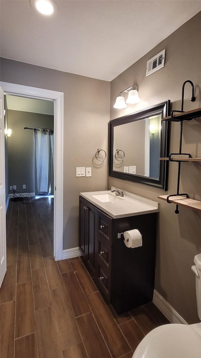 bathroom featuring toilet, wood finish floors, vanity, visible vents, and baseboards