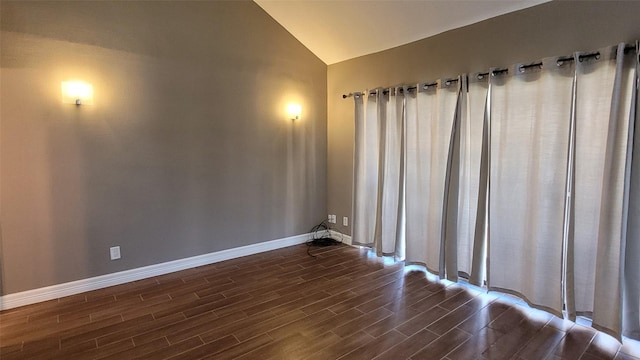 spare room with lofted ceiling, baseboards, and dark wood finished floors