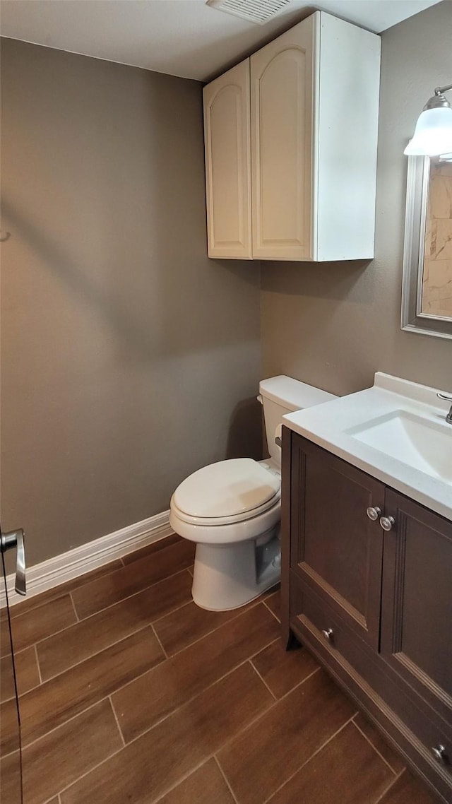 half bathroom featuring wood finish floors, toilet, vanity, and baseboards