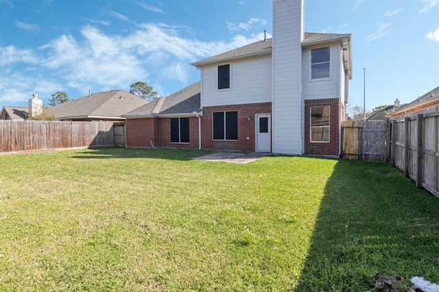 rear view of house with brick siding, a lawn, a chimney, and a fenced backyard