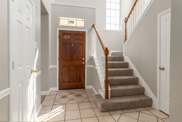 foyer entrance with light tile patterned floors, stairs, and baseboards