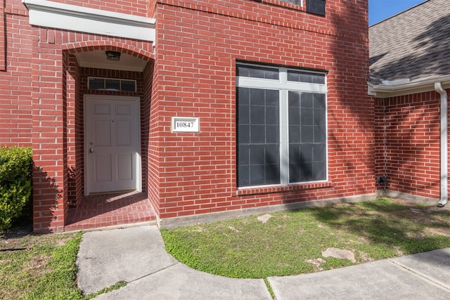 view of exterior entry with brick siding and roof with shingles