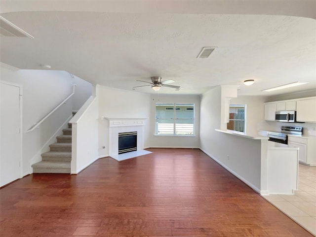 unfurnished living room with stairway, a ceiling fan, visible vents, light wood finished floors, and a fireplace with flush hearth