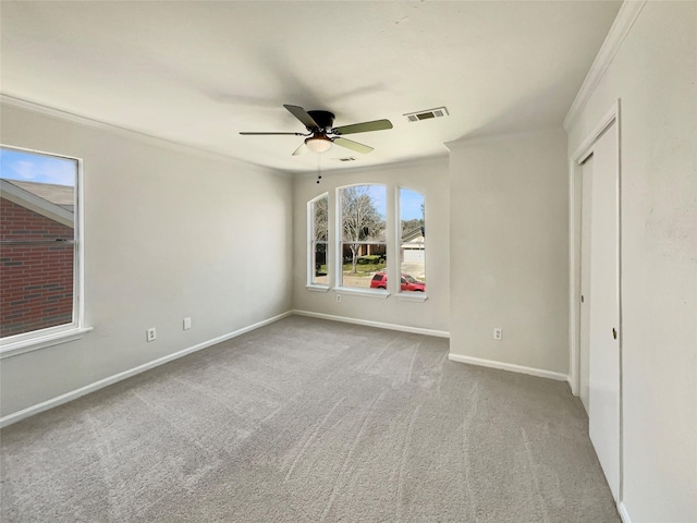 carpeted empty room with visible vents, baseboards, ornamental molding, and a ceiling fan