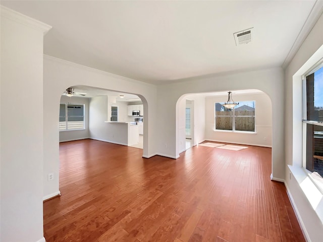 unfurnished living room with visible vents, ceiling fan, baseboards, wood finished floors, and arched walkways